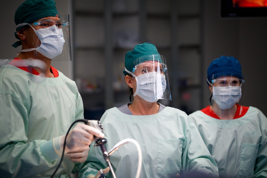 Three people in surgical gear.