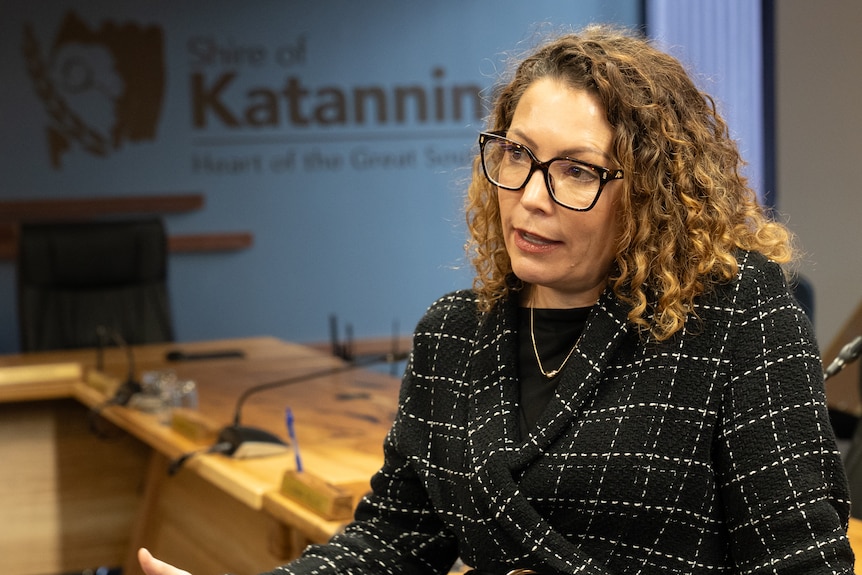 A woman in black-rimmed glasses and a dark suit being interviewed