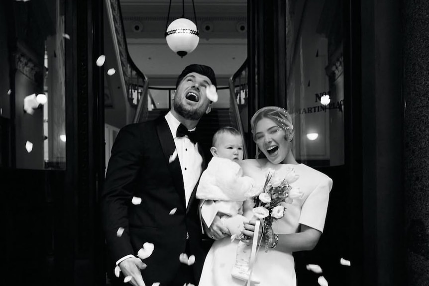 A man and woman in wedding clothing holding a baby and smiling.