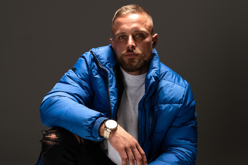 Producer Needs No Sleep crouching and leaning on a knee, blue puffer jacket on