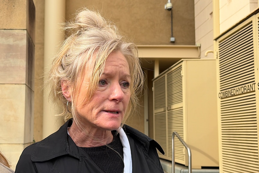 Two women stand in front of the Coroner's Court to speak with a media scrum. 