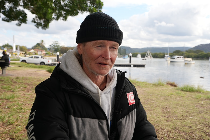 A man in a black jacket and beanie sitting at a park.