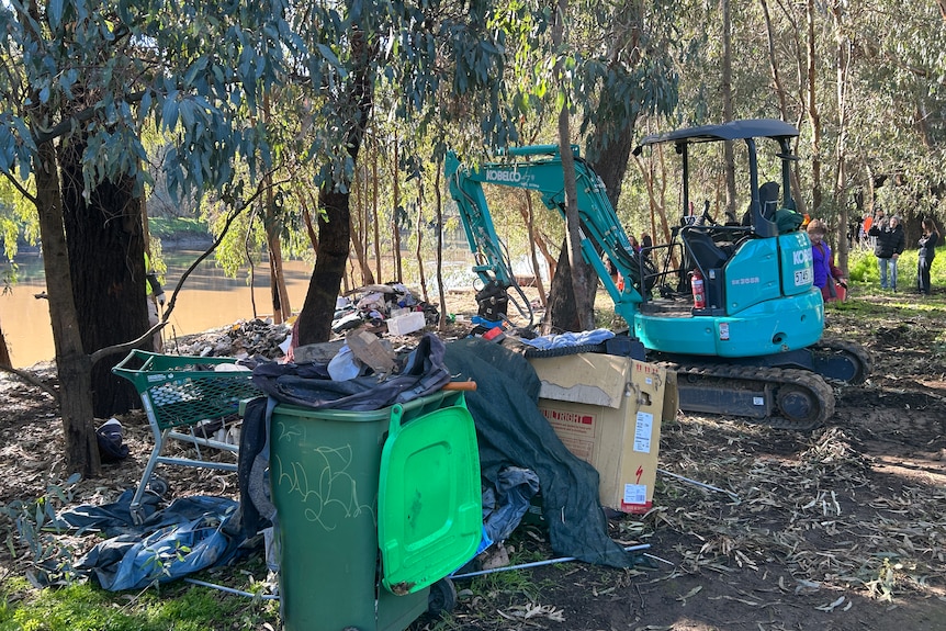Excavator pictured next to a trolley and camp items, with the backdrop of Wagga beach