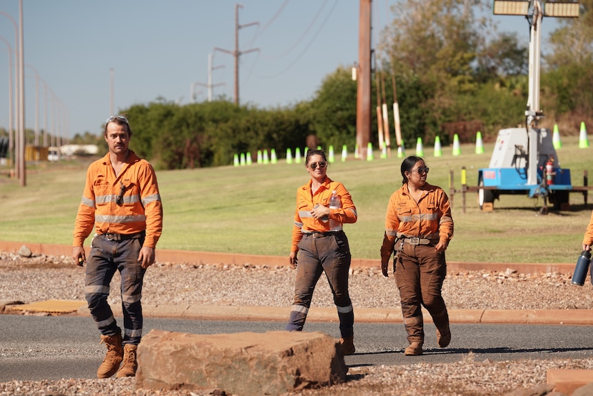 Three people in orange uniforms walk across a road.