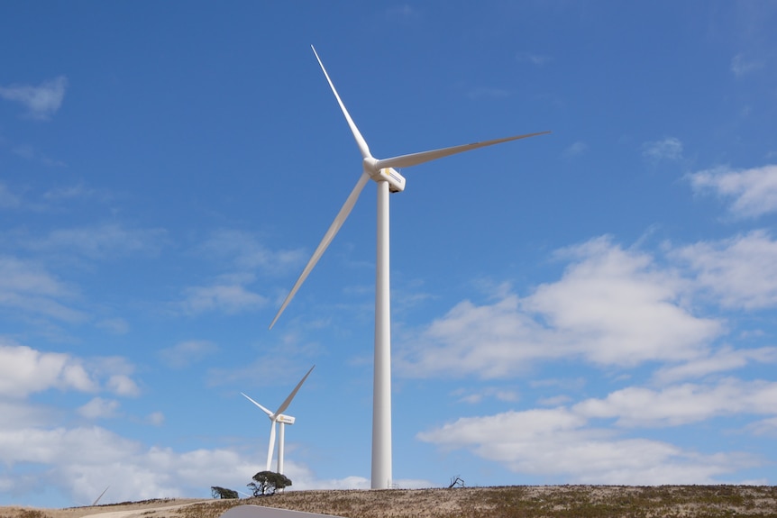 A large wind turbine with another just behind it on a brown hill with a blue sky