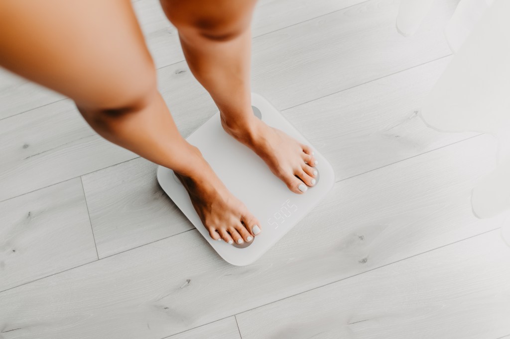 Feet of a young woman on a digital weighing scale showing 59.05.