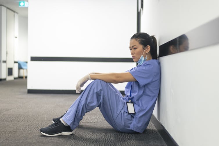 A female nurse of asian descent sits on the hospital hallway floor.