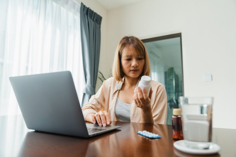 Young woman hold medicine searching information online by laptop in living room at home.
