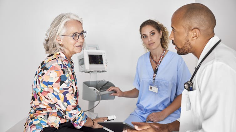 A female patient sits on an exam table, talking with a doctor and nurse