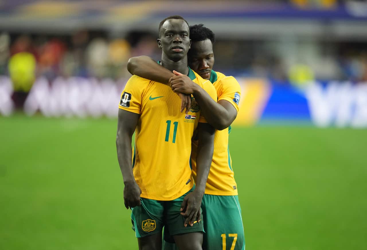 Two men in yellow and green jerseys sadly hug