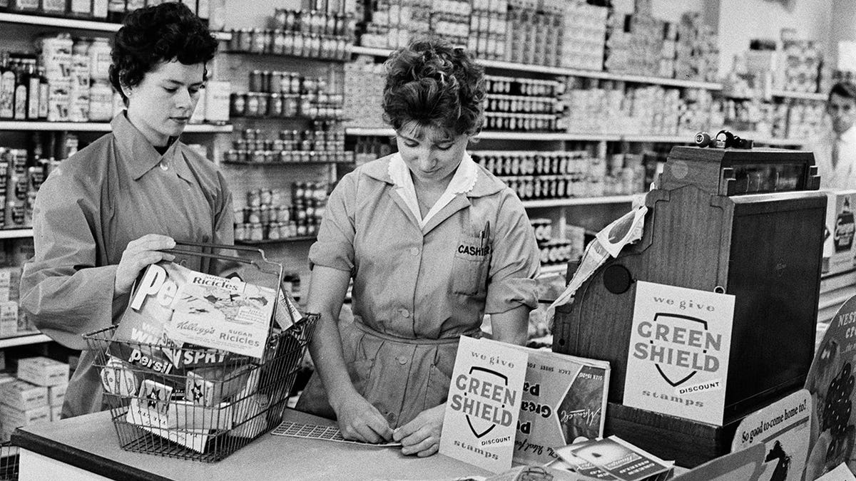 Shop assistant hands Green Shield stamps to a customer in a supermarket.