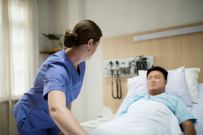 A hospital employee, a nurse, attending to a patient in a hospital bed, hinting at hospital horror stories.