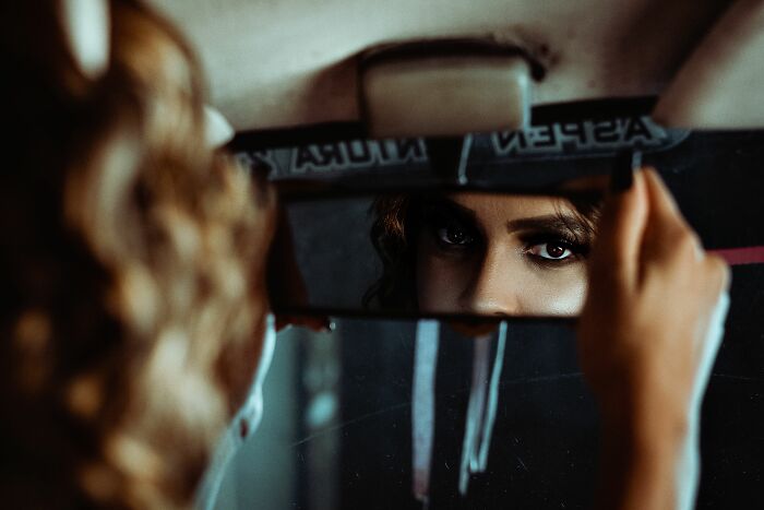 A woman's intense eyes are visible in a car's rearview mirror, hinting at unsettling horror stories.