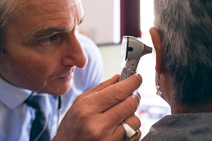 A doctor examining a patient's ear with an otoscope, checking for medical symptoms.