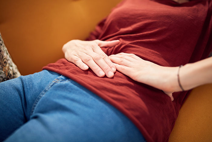 A person lying on a couch holding their stomach in discomfort, a medical symptom doctors wish people would not ignore.
