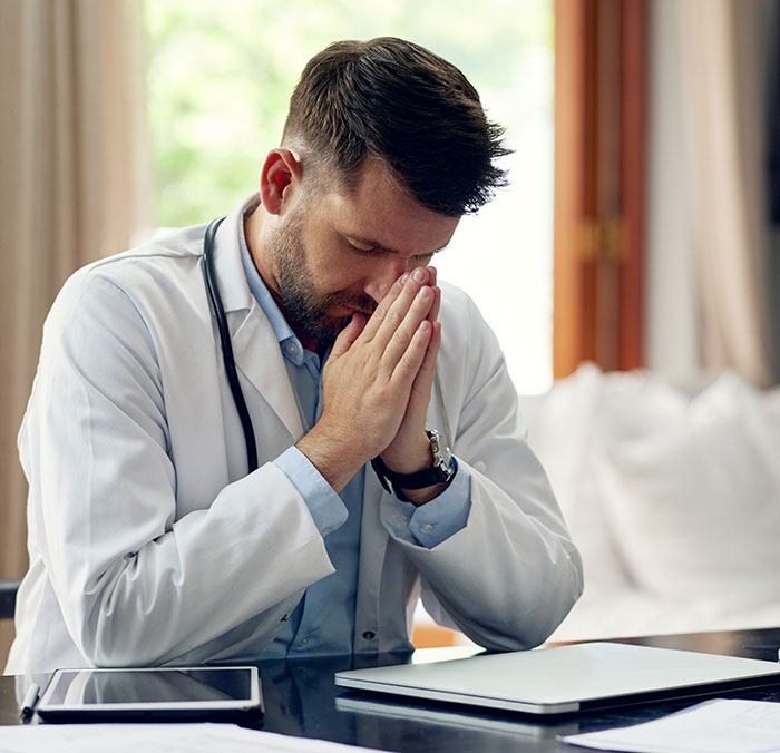 A doctor sitting at a desk with his hands clasped, illustrating medical symptoms doctors wish people would not ignore.