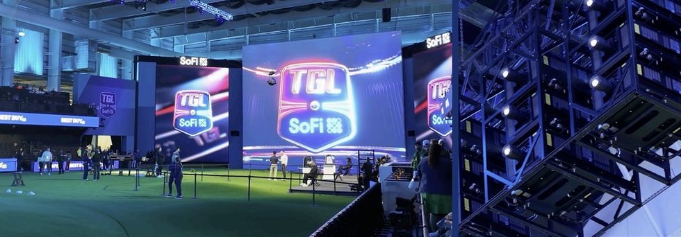 Indoor golf event setup with large screens displaying "TGL" and "SoFi" logos.