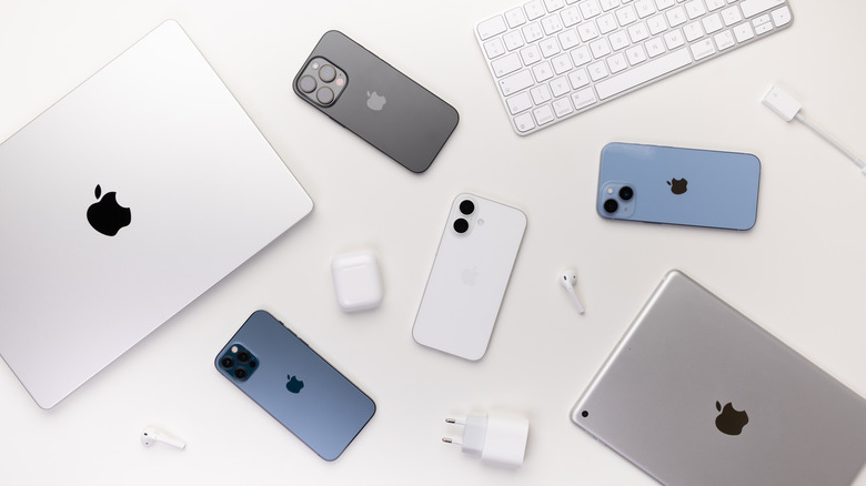 Collection of Apple gadgets, including iPhones, MacBooks, an iPad, AirPods, a keyboard, and a charger, on a white background.