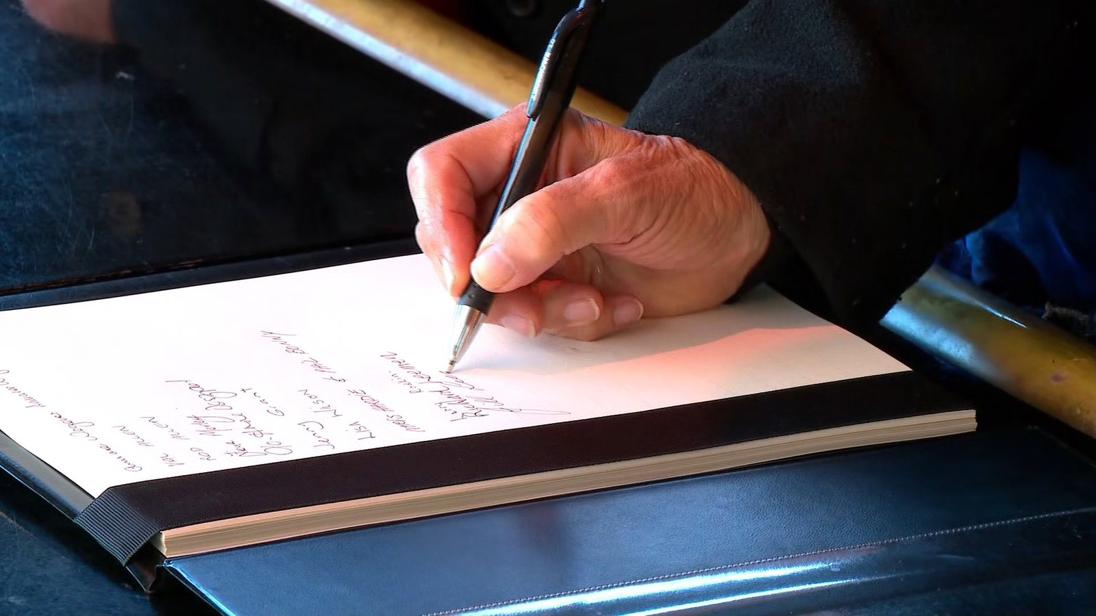 An up close of someone writing in a leather bound book a message. The writing isn't distinguishable.