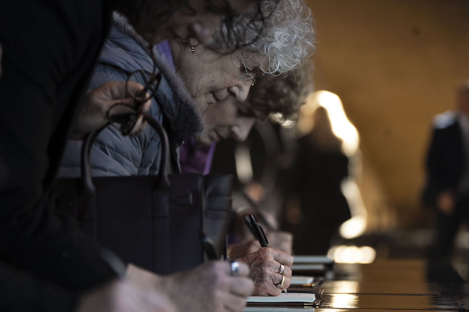 An up close of an older woman writing in a leather bound book a message. The writing isn't distinguishable.