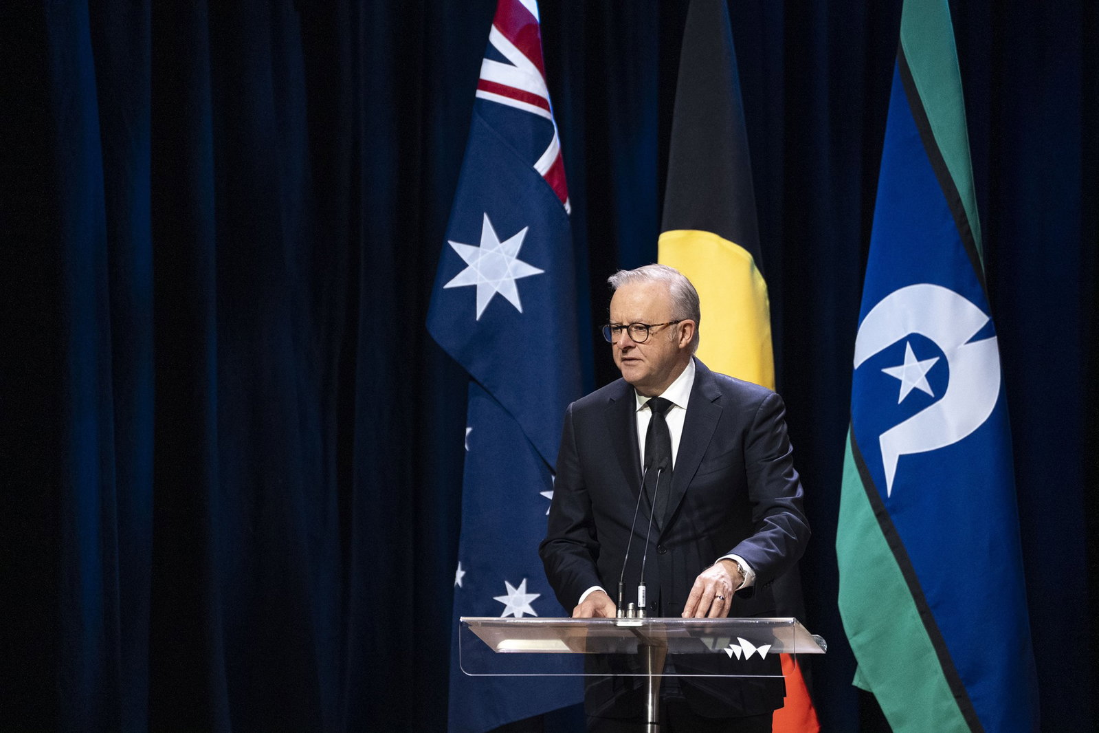 Anothony Albanese talking in front of Australian and Indigenous flags.