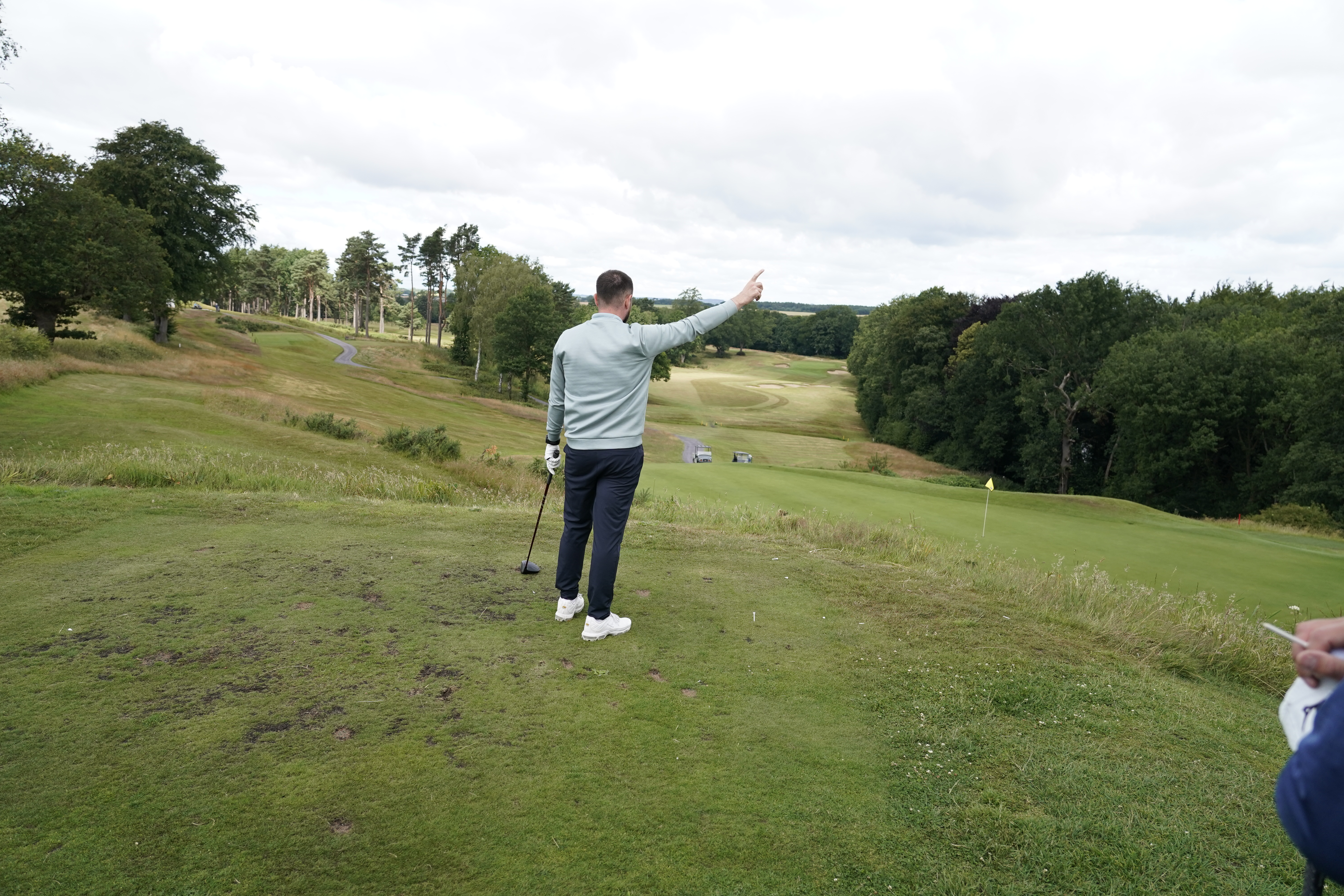 Baz Plummer pointing right on the tee to indicate a ball flying out of bounds due to a slice with driver