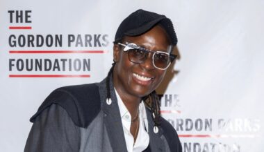 A smiling person in glasses and a dark cap poses in front of a backdrop that reads "The Gordon Parks Foundation.