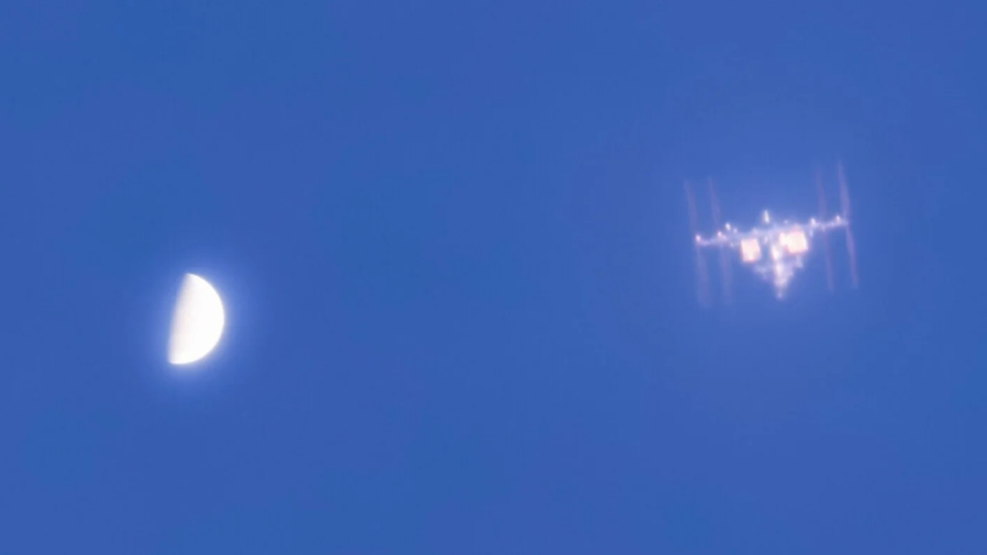 a T-shaped space station beside a half-orb on a blue sky
