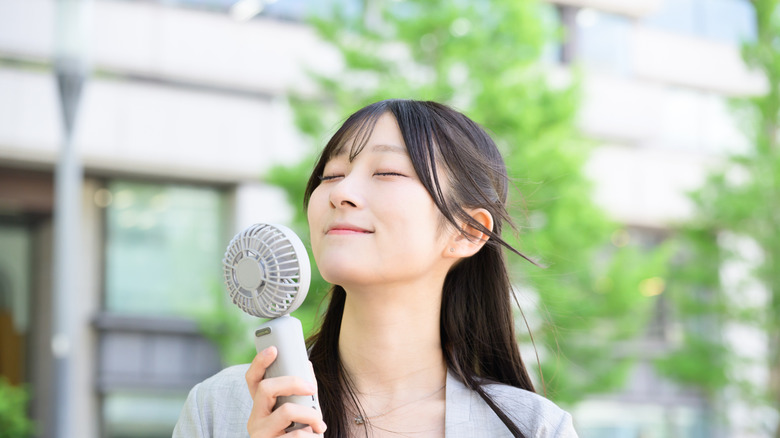 A woman smiling as she holds a handheld fan to her face