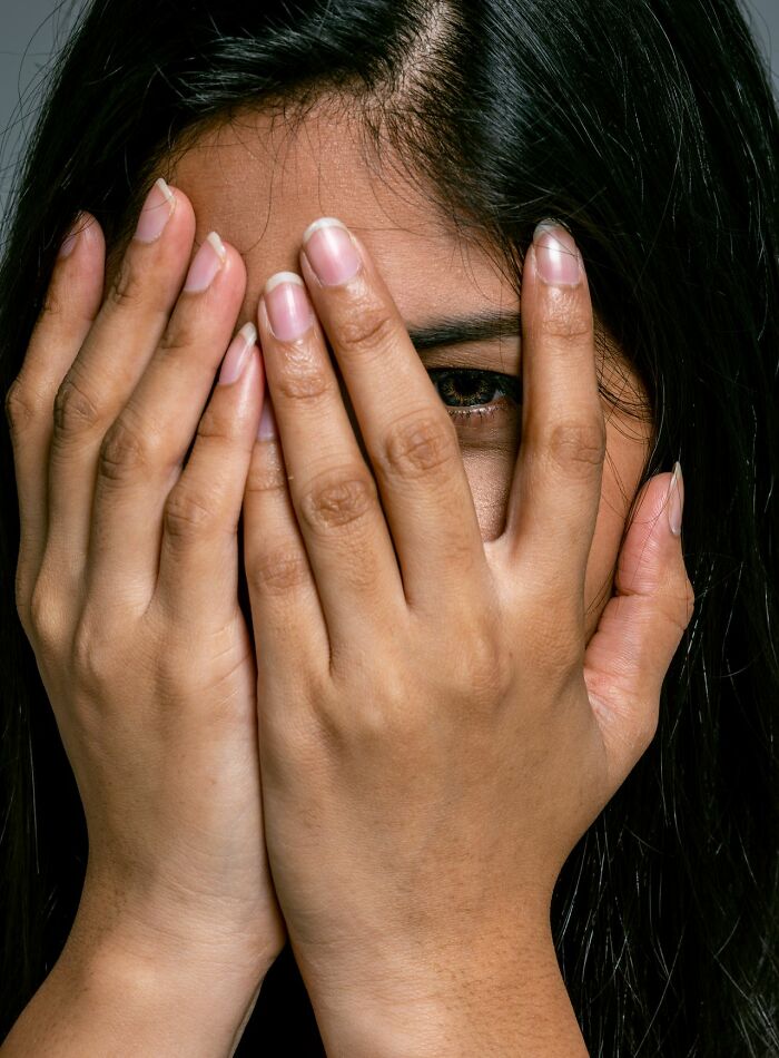 A woman covers her face with her hands, one eye peeking out, illustrating ridiculous patients ER staff encounters.