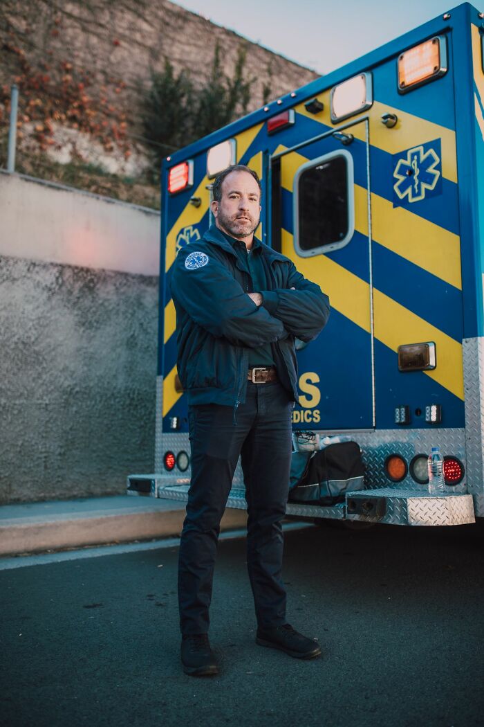 An ER staff member, a paramedic, standing with crossed arms in front of an ambulance.