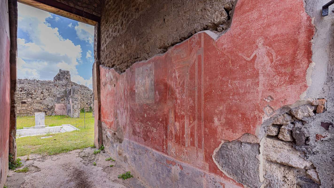 A view of ancient wall frescoes and ruins through an open doorway.