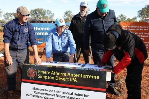 A group of people signing documents on a desk set up in the Simpson Desert