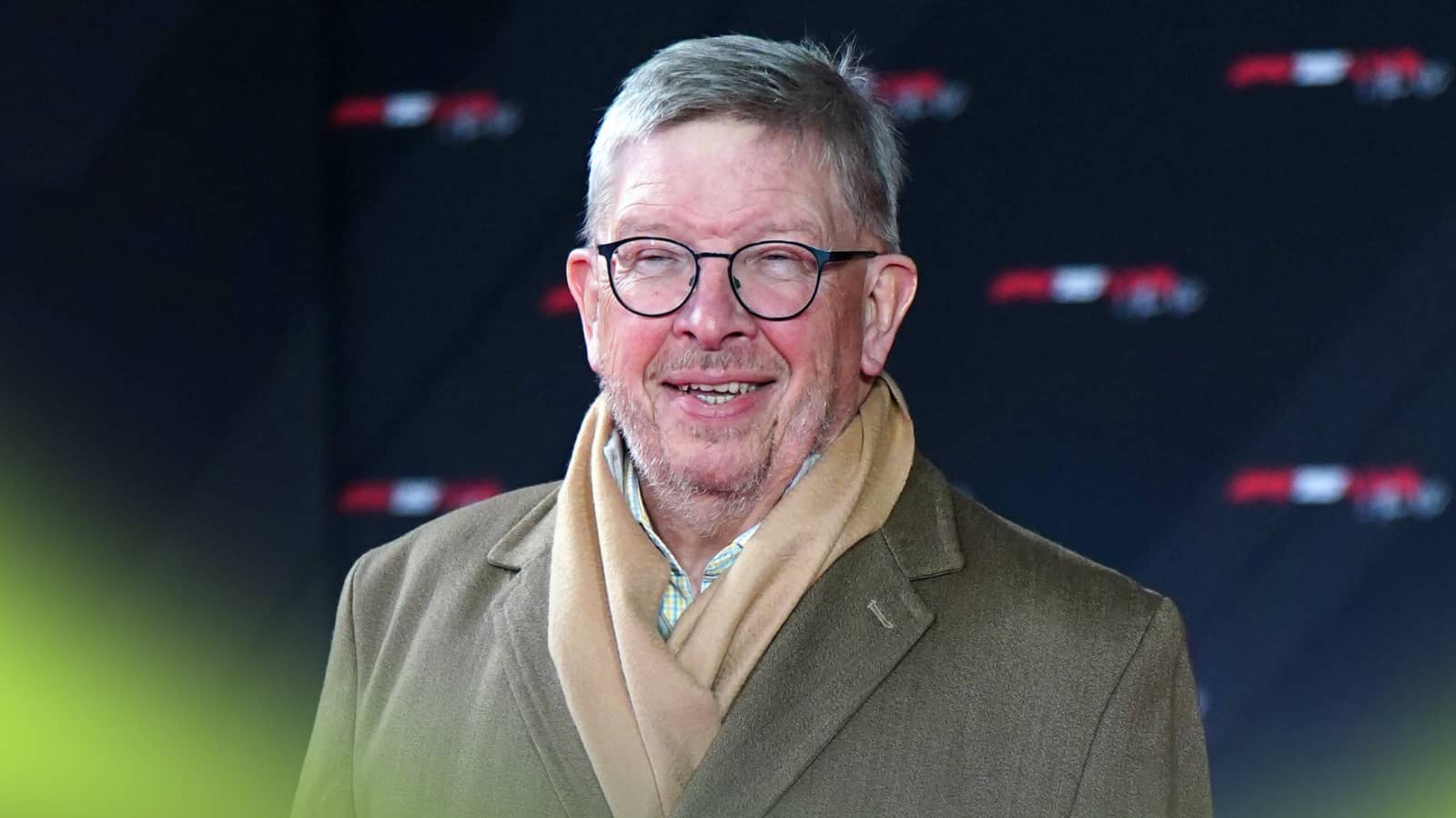 Ross Brawn smiles broadly while wearing a coat and scarf