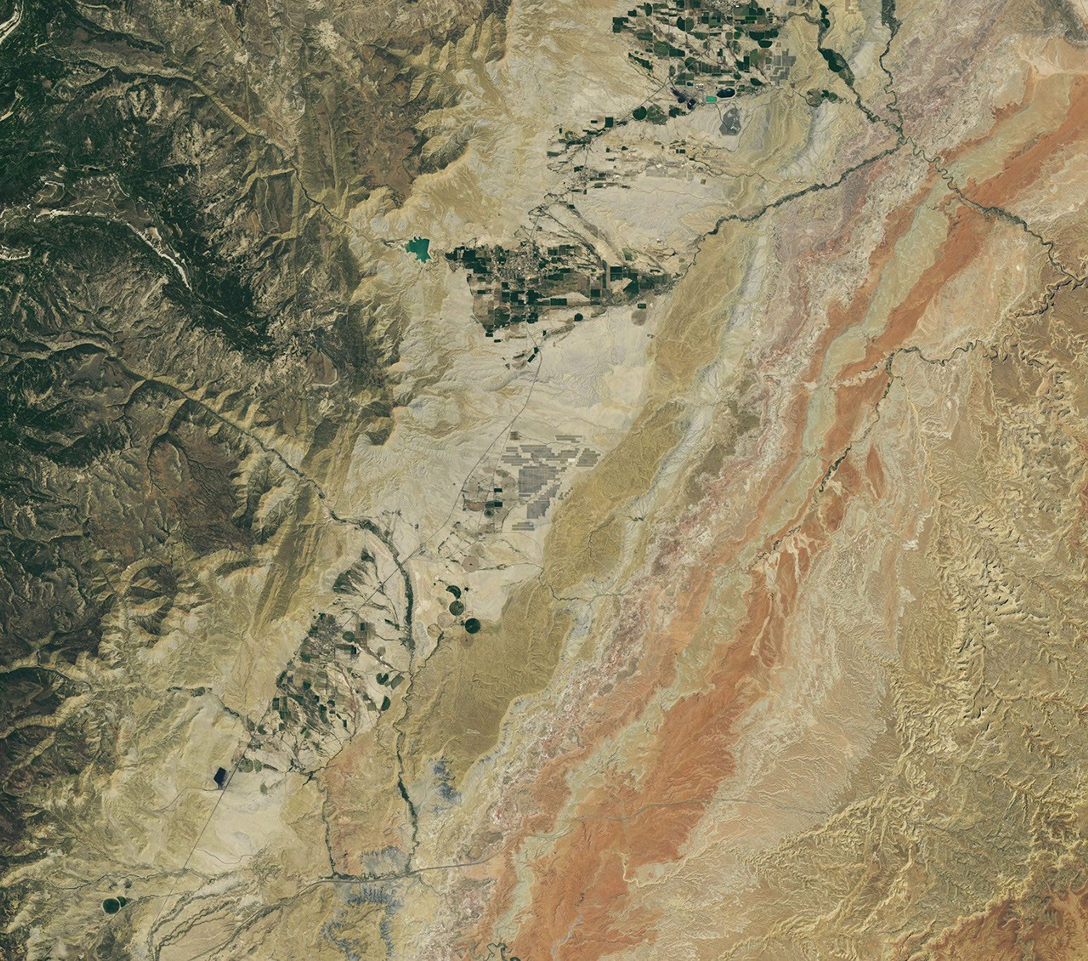 Grid-like arrays of solar panels cover parts of a valley floor in a brown, dry-looking area of Utah.