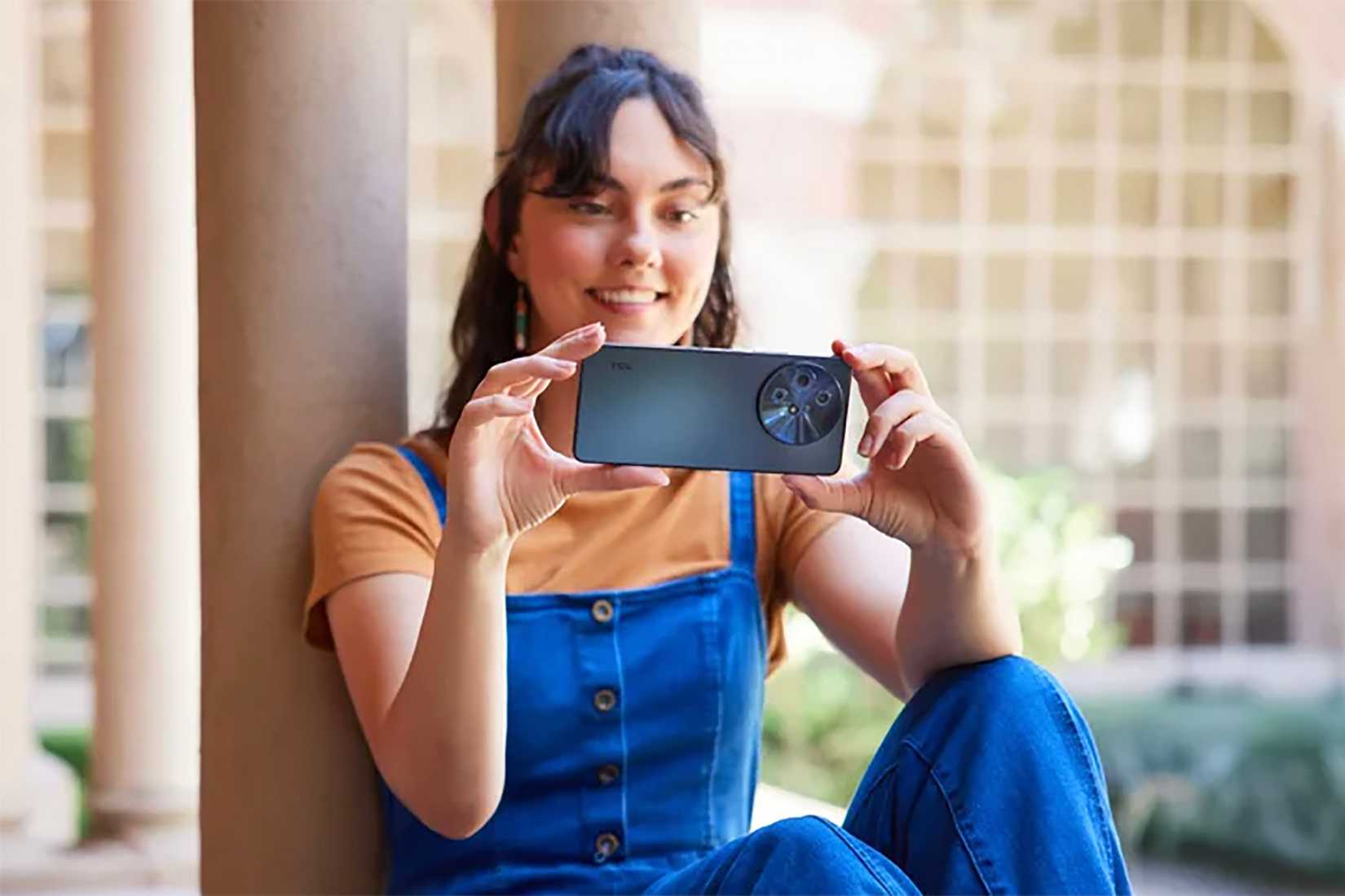 A woman sitting down holding the TCL 60 XE NxtPaper phone vertically. 