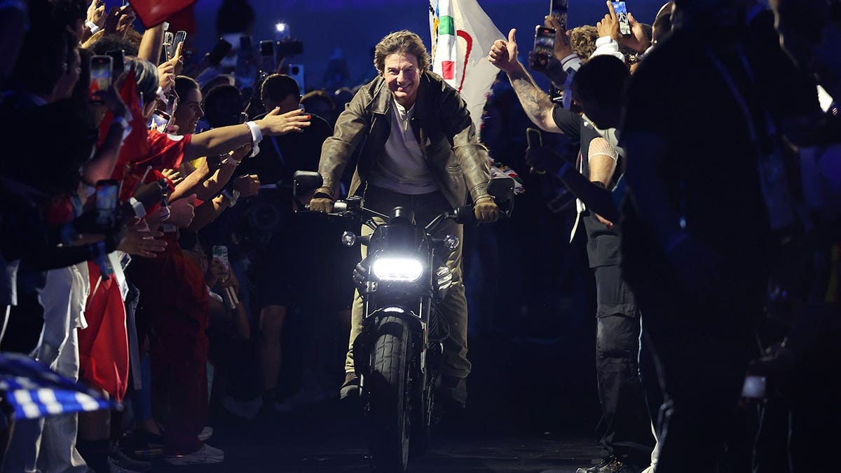 Tom Cruise riding a motorcycle as fans reach out from the sidelines