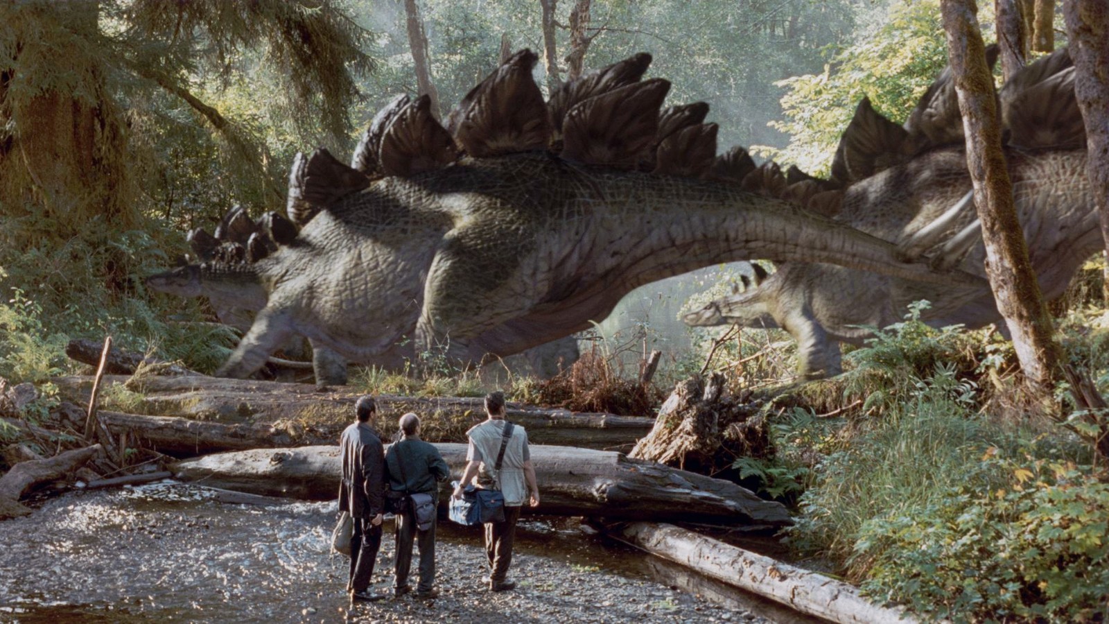A family of giant, four-legged dinosaurs, their back lined with triangular plates, are crossing a river in a jungle. Standing in the foreground are 3 adventurers, staring up in awe.