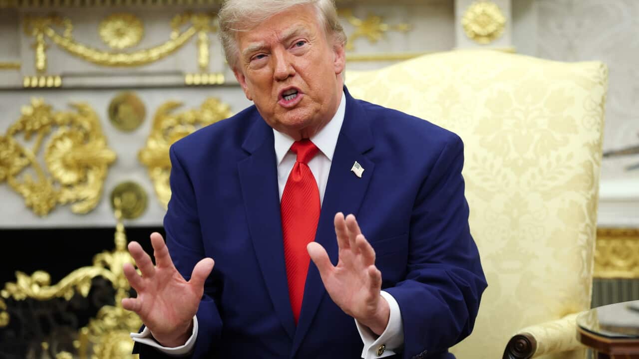 Doanld Trump sitting in a yellow chair, in a room with gold plating on the white walls. He is waving his hands.