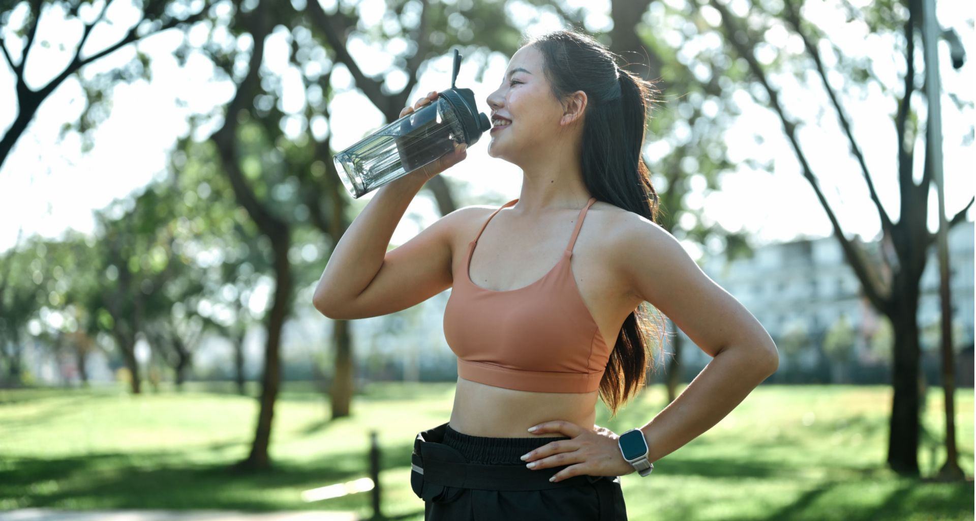 woman in sports bra and leggings outside in front of grass and trees drinking water out of water bottle, when to drink on runs
