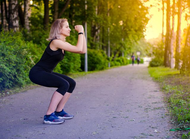 Girl squatting. Healthy lifestyle. Exercises. Sports in the fresh air. Squat. Muscle tone. Speed. Blonde woman in sports clothes black. Photo. The radiance of the sun.