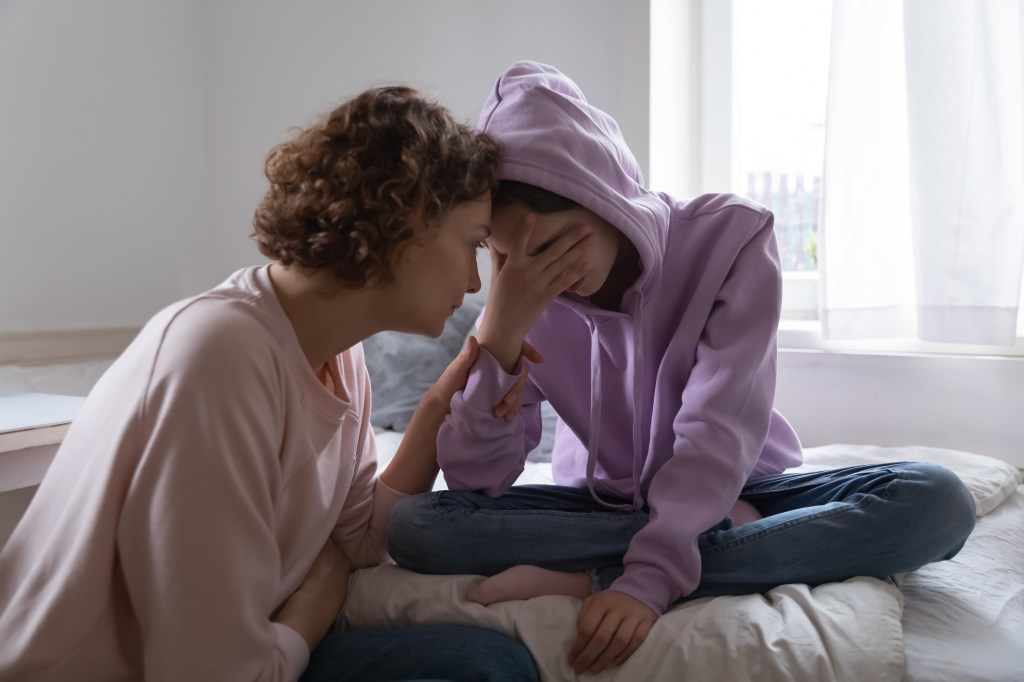 A worried mother comforting her crying teen daughter at home.