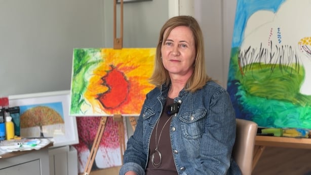Woman wearing denim jacket sits surrounded by art work