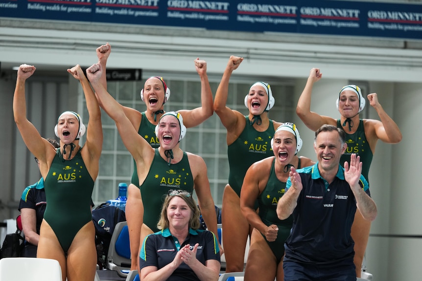 Australian water polo players on the bench hold up their hands and cheer