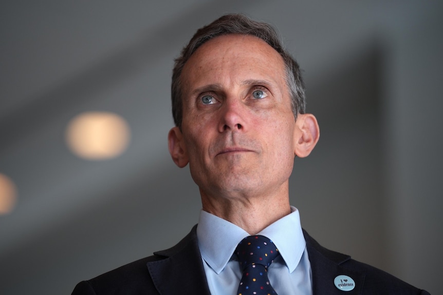 a close-up of a middle-aged man wearing a suit looking serious inside a foyer