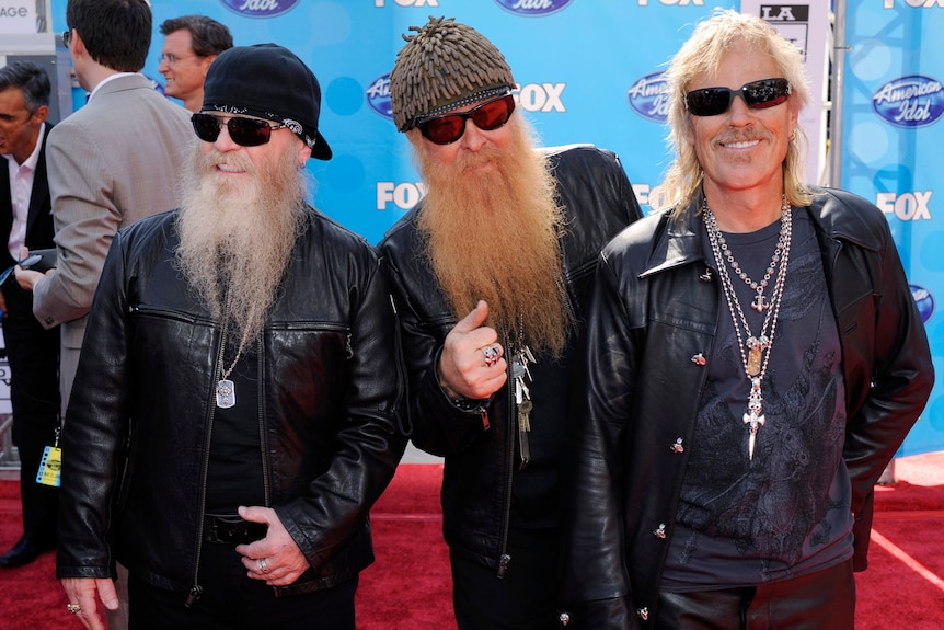 Three men stand on a red carpet. 
