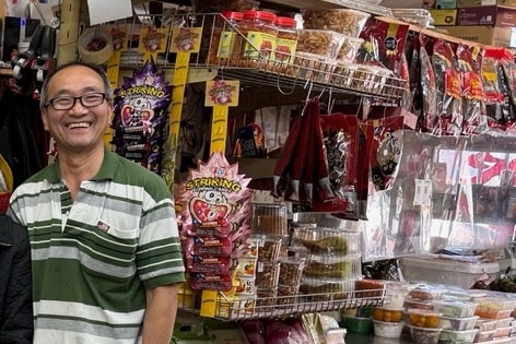 A smiling 60 something Asian man stands in front of b