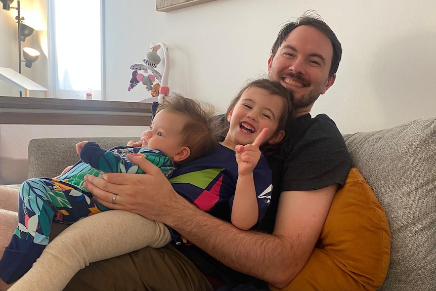 A man sitting on a sofa with two young children on his lap.
