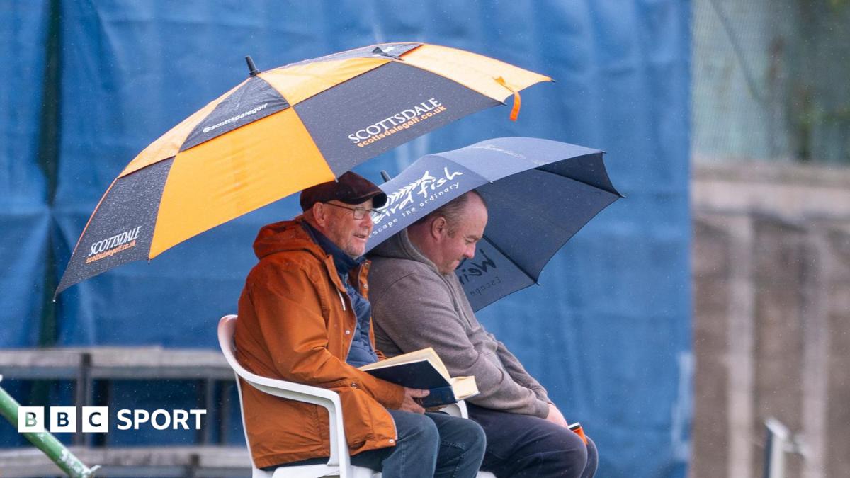 Two spectators hold up umbrellas in the rain at Forfarshire Cricket Club
