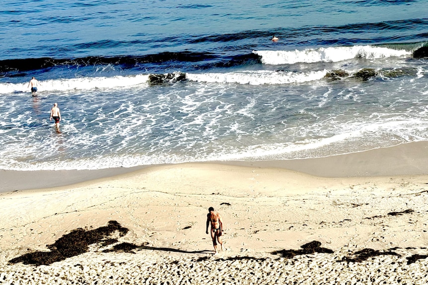 A man walks up the sand away from the water on North Cottesloe Beach foreshore.